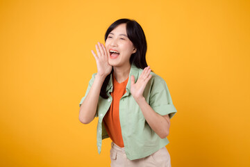 Energetic young Asian woman in her 30s wearing a green shirt on an orange background, shouting with excitement. Explore the concept of discount shopping promotion with this vibrant image.