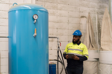 Factory male engineer worker working and using digital table checking tank of air compressor in industry factory. Male technician checking or maintenance air compressor machine in plant