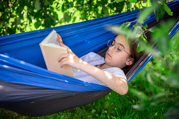 Cute girl reading a book in a hammock in the garden.