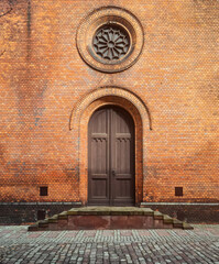 Fototapeta na wymiar Side facade entrance into catholic church. Veranda porch with a wooden door and round rosette window above it