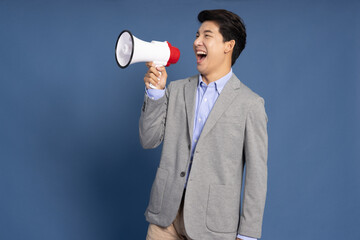 Young Asian business man shout loudly and holding megaphone isolated on blue background, Speaker...