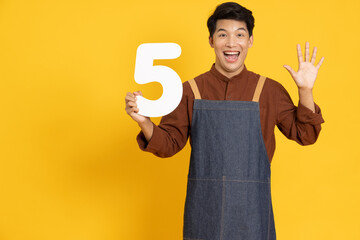 Restaurant owner sme young Asian man holding number 5 or five isolated on yellow background