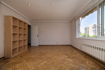 Empty living room with a wooden colored bookcase on one wall and a large sliding window on the other