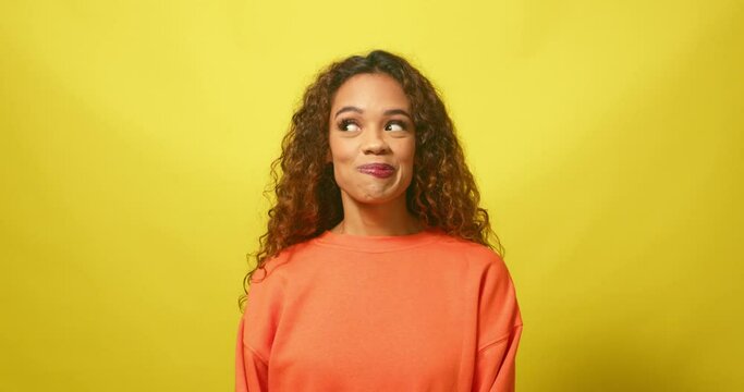 Cute young woman pulls funny faces, nervous and shy, yellow studio background
