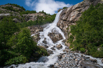Fototapeta premium View of the Alibek waterfall formed by the fall of the Jalovchatka River from the Alibek glacier on a sunny summer day, Dombay, Karachay-Cherkessia, Russia