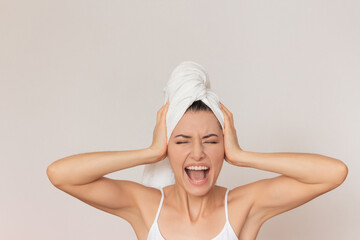 close-up photo of a young pretty woman in white underwear with a white towel has closed her eyes and presses her hands to her head, spreading her elbows to the sides, screams,  covering her ears