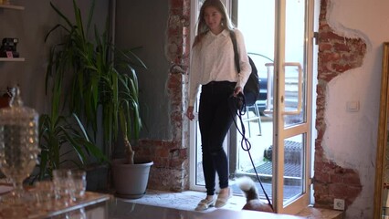 4k Woman walks into cafe with dog spbd. Young european female owner holding cute pet on leash and looking with smile, coming in interior. Beautiful redhead lady leads adorable furry animal and visits