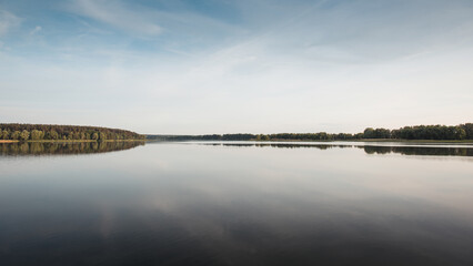 Summer scene on lake: refection of forest trees in the water of pond. Warm summer evening on sunset.