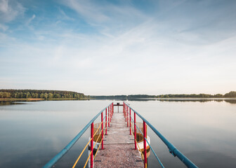 Summer scene on lake: symmetric photo of jetty and reflection of forest in the background