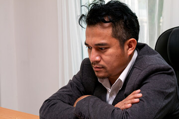 Stressed Asian Businessman sitting at Office Desk: Overwhelmed with Serious facial Expression