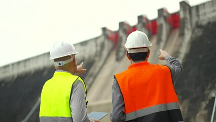 Confident asian two maintenance engineers man inspection with in tablet at construction site dam with hydroelectric power plant and irrigation. Team engineer man working at project big building.and ir - Powered by Adobe