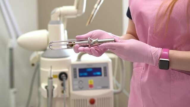 Close-up of the hands of a female doctor gynecologist in pink medical gloves, holding metal tools, nozzles for Fotona laser gynecology. copy space. The concept of laser gynecology.