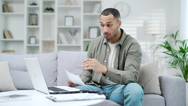 Confused man because of expenses utility bills or from invoice have no money to pay mortgage or loan. High prices and spending money calculating finances sitting at home with a calculator and laptop