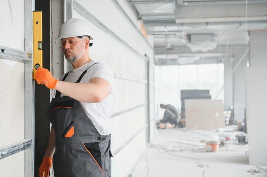 man drywall worker or plasterer putting mesh tape for plasterboard on a wall using a spatula and plaster. Wearing white hardhat, work gloves and safety glasses. Image with copy space.