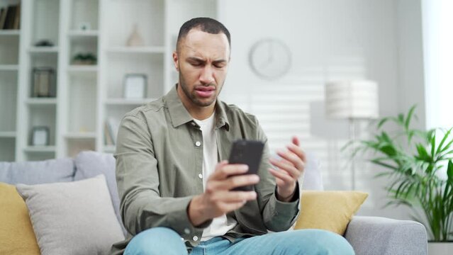 Angry unhappy man user because of phone failure problems, spam, non-working app, no Wi-Fi connection. breakdown use smartphone service fail bad signal poor internet while sitting at home room indoor