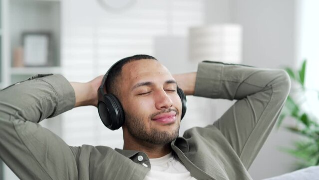 Tired arabian man take break work at home wear headphones listen relaxing music. Exhausted businessman male in headset relax peaceful melody song peace calm serene stress free rest on couch Closeup