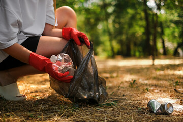 a woman in gloves walks in the park and collects plastic in a trash bag