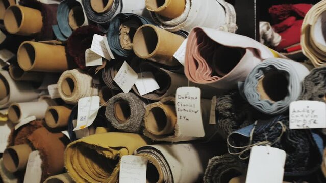 Rolls of fabric and textiles for sale stacked on shelves in shop. Close -up Warehouse various fabric, slow motion.