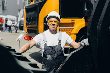 Happy Industrial worker male senior in helmet on background of production of excavator, working on industry factory