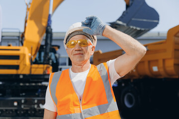 Happy Industrial worker male senior in helmet on background of production of excavator, working on...