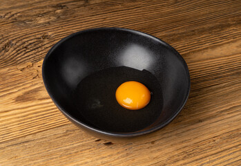 One Broken Egg in Black Bowl, Raw Yolk and White, Fresh Broken Organic Chicken Egg