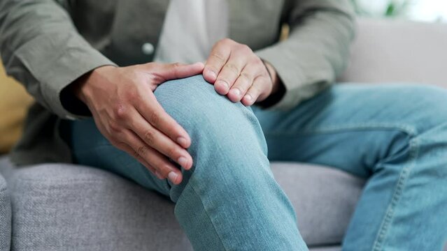 close up of hands massaging an injured knee or joint legs Pain Person mixed race man Experiencing Discomfort Trauma or Arthritis Injury muscle cramp sit at home room on the sofa indoor closeup 