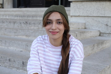 A young fashionable woman in her twenties is wearing a green beanie and a pink/white striped shirt