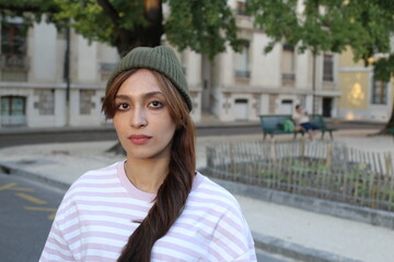 A young fashionable woman in her twenties is wearing a green knitted hat and a pink/white striped shirt
