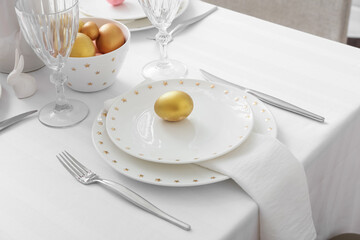 Beautiful table setting with golden Easter eggs in room, closeup