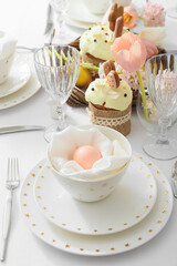 Beautiful table setting with Easter egg, cakes and tulip in room, closeup