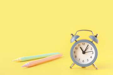 Alarm clock and pens on yellow background