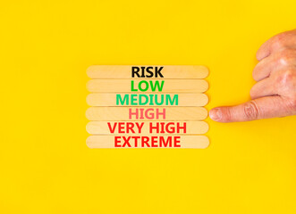 Time to high risk symbol. Concept word Risk low medium high very high extreme on wooden sticks. Businessman hand. Beautiful yellow background. Business time to high risk concept. Copy space.