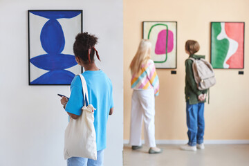 Back view at diverse group of teenagers looking at abstract art in modern art gallery or museum, copy space