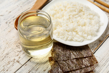 Obraz na płótnie Canvas Plate with boiled rice, vinegar and nori sheets on light wooden background, closeup