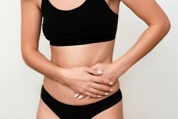 a young Caucasian woman in black underwear holding her hands in pain by the side of her stomach isolated on a light background. Gynecological problems. Stomach pain. Women's Health