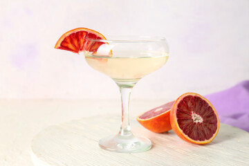 Glass of tasty martini and red orange on white wooden table