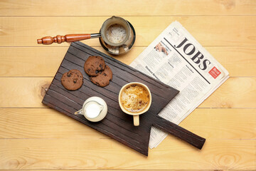 Board with cup of coffee, milk, cookies, cezve and newspaper on light wooden background