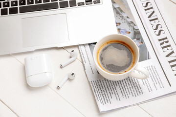 Cup of coffee with earphones, newspaper and laptop on white wooden background, closeup
