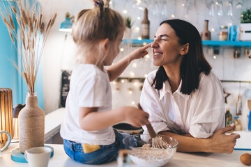 Cheerful woman enjoying fun with daughter in kitchen