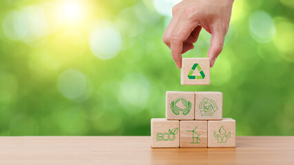 Hand holding wooden cube block with recycle, earth, eco friendly and green energy icon in green...