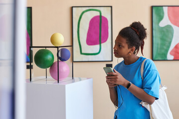 Colorful portrait of African American teenage girl looking at abtract sculpture in modern art...
