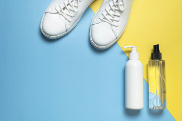 White leather sneakers, plastic bottles of cleaning products for shoes on blue yellow background flat lay top view. Natural leather shoe care, spray, foam, shoe deodorant, cosmetic shoe products
