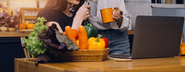 Happy couple using laptop computer preparing healthy food diet vegetable salad at home together. Woman and man are searching recipes, ordering shopping online, watching cooking class in kitchen.