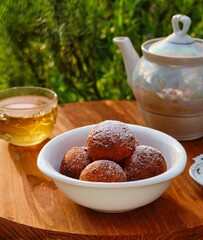 Round cottage cheese donuts, sprinkled with powdered sugar, in a white bowl on a round wooden background. Donut recipes.