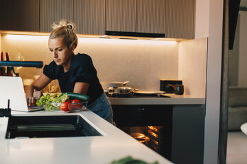 Woman watching tutorial on digital tablet and cooking at home