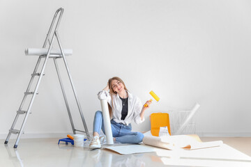 Young woman with wallpaper and roller sitting in room