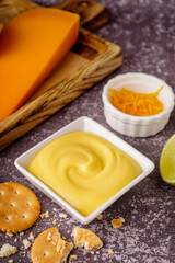 Bowl of tasty cheddar cheese sauce with crackers on black grunge background