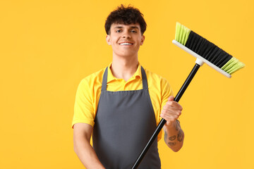 Male janitor with broom on yellow background