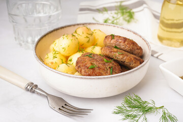 Bowl with cutlets, boiled baby potatoes and dill on white table in kitchen