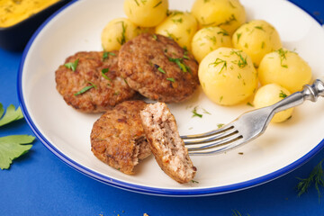 Plate with cutlets, boiled baby potatoes and dill on blue background
